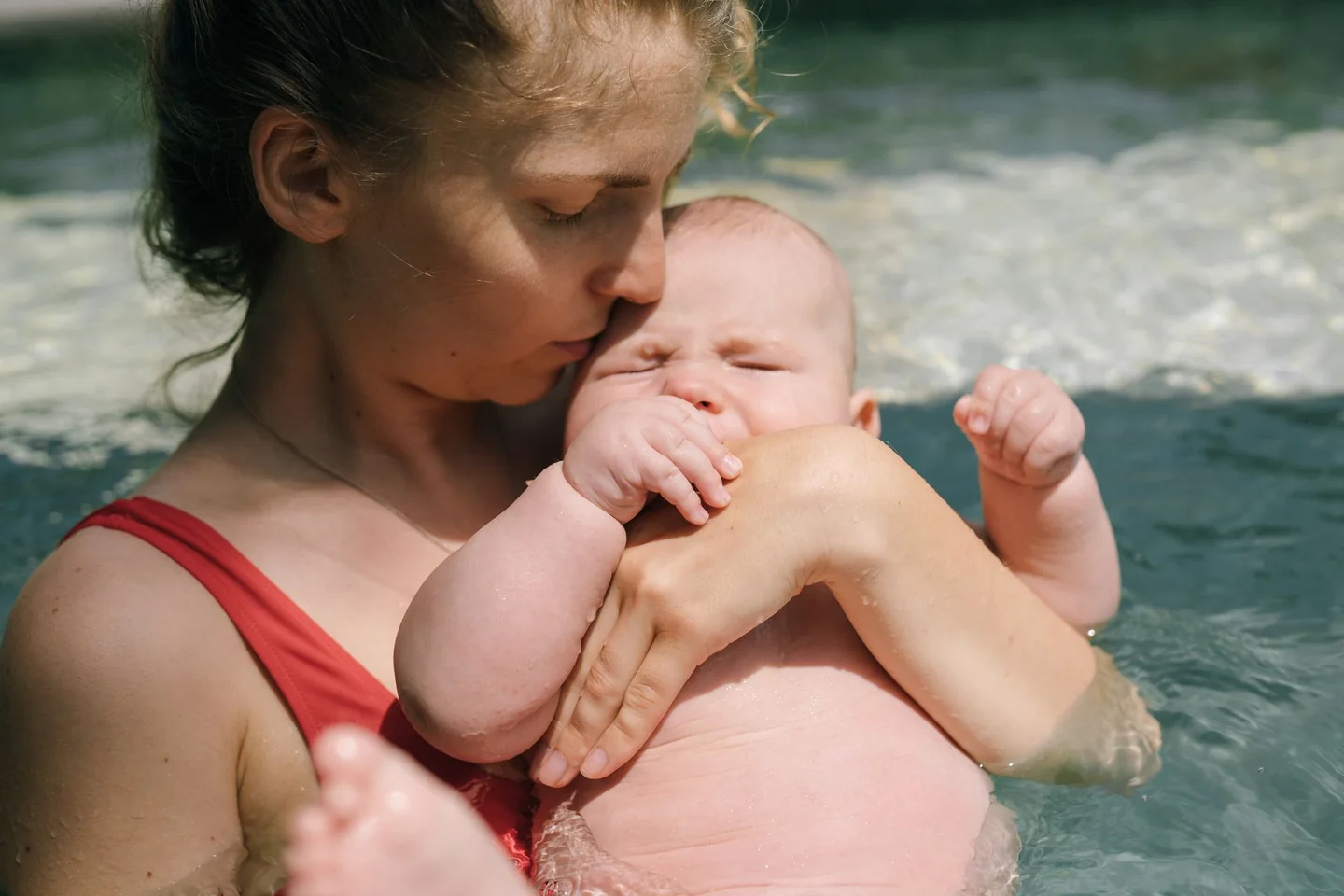 Mère maintenant son bébé contre elle dans une piscine extérieure