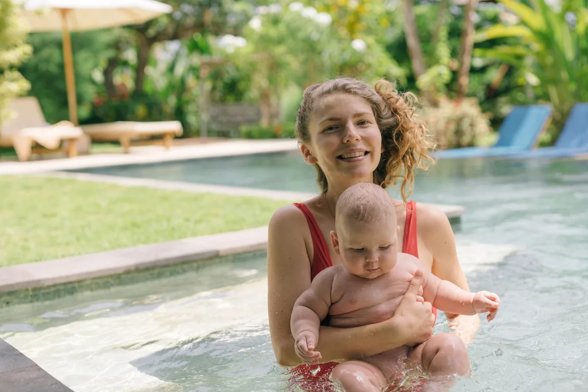 A smiling mother and her baby enjoying a sunny day in an outdoor pool, embracing togetherness